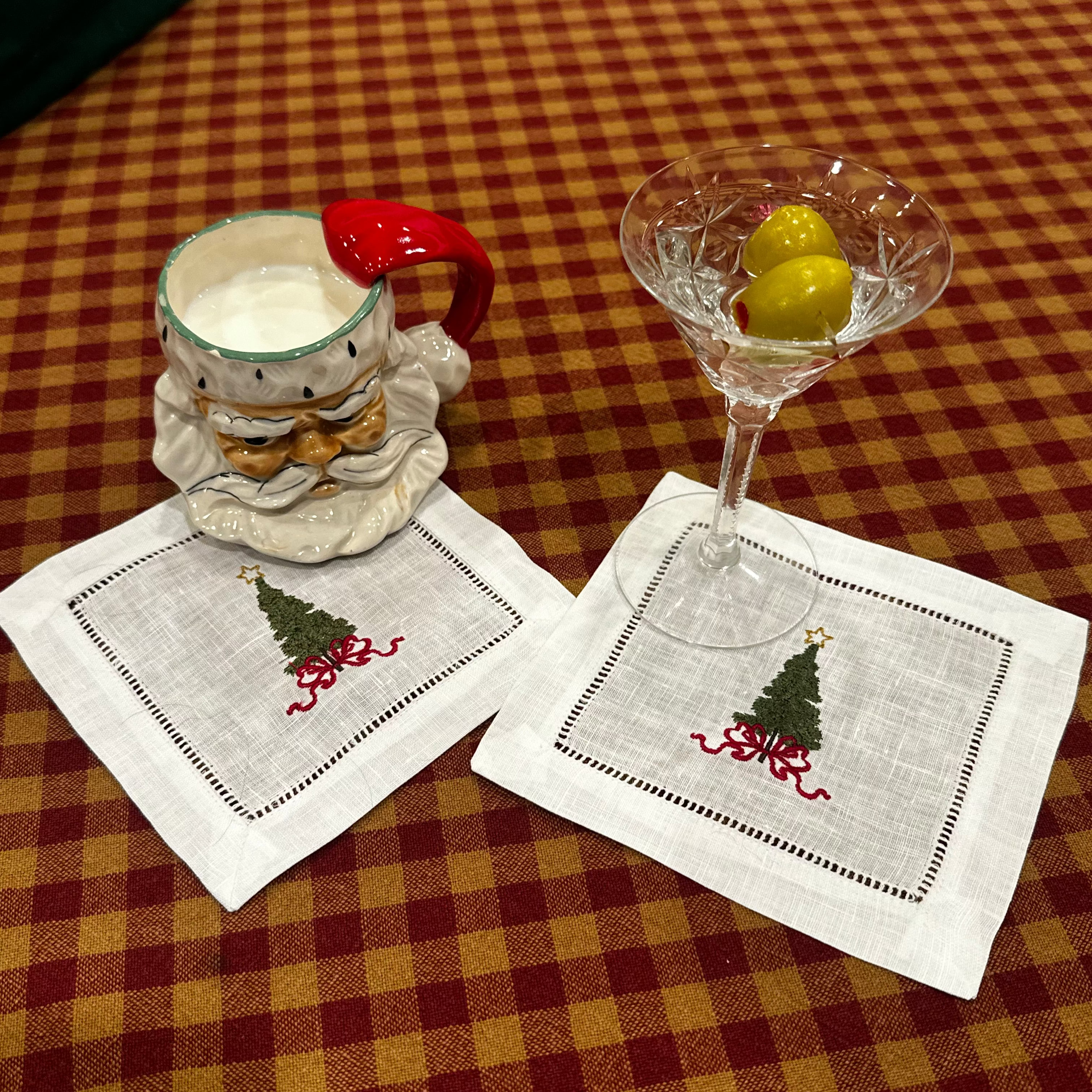 Two custom cocktail napkins with Christmas tree designs on a checkered tablecloth.