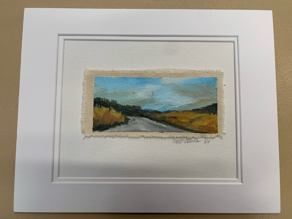 Small landscape painting in a white frame on a brown background