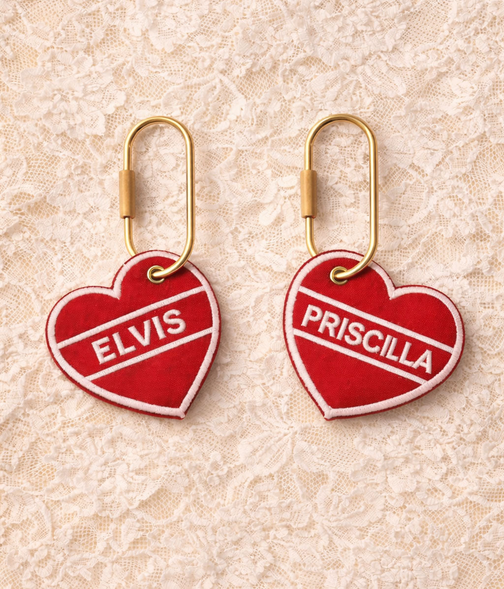 Heart-shaped keychains with 'Elvis' and 'Priscilla' text on a textured beige background